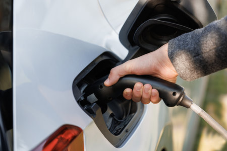 Close up of hand attaching power cable to environmentally friendly zero emission electric car. Businessman plugging electric car from charging station. Senior plugging in power cord to electric carの写真素材