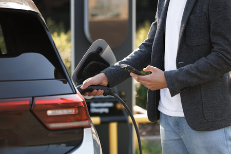 Unrecognizable man plugging electric car from charging station. Male plugging in power cord to...