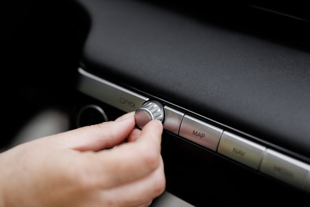 Car dashboard volume knob. Drivers hand adjusts volume control of car radio. Female hand control...