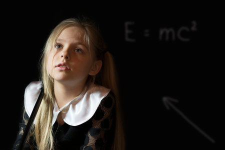 little girl standing at the blackboard on which is written the formula of energy