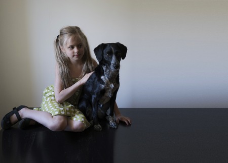 girl with her dog sitting on a shiny black floor against a white wallの写真素材