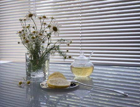 a bouquet of daisies in a glass vase, honey, lemon on a table on a background window. still life in whiteの写真素材