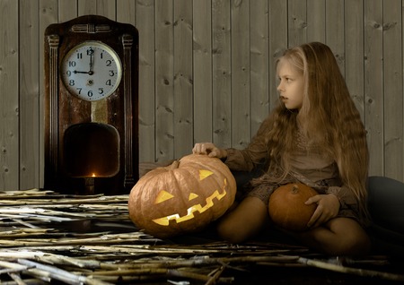 vintage, children. cute little girl sitting next to a pumpkin glowing and looks at the clockの写真素材