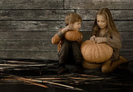 Pretty blond girl and the boy sitting next to a large pumpkin and talkの写真素材