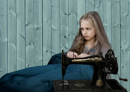vintage children. girl sews blue dress on an old sewing machine