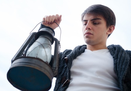 young man with a kerosene lamp in his hand against the skyの写真素材
