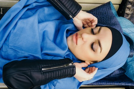 young girl in a blue scarf lying on a park benchの写真素材