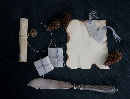a sheet of paper, pine cones and silver antique knife on dark background. top viewの写真素材