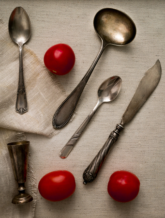 antique silver cutlery and cherry tomatoes on canvasの写真素材