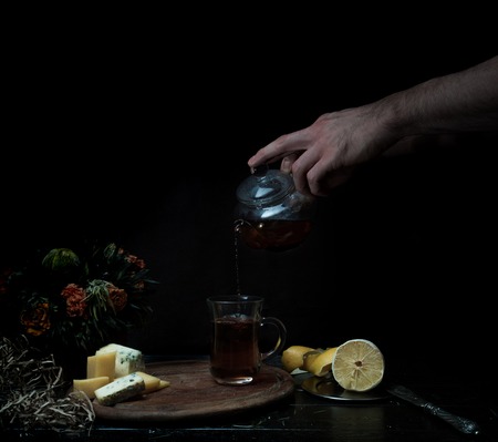 male hands pour tea in transparent cup. dark background, vintageの写真素材