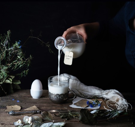 female hand is pouring milk from a jug into a glass. dark background.の写真素材