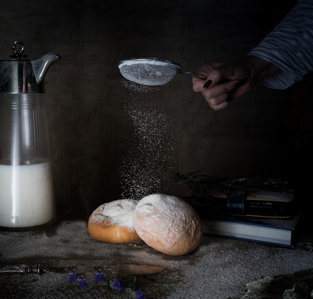 female hand sifts the flour on a wooden table. dark backgroundの写真素材