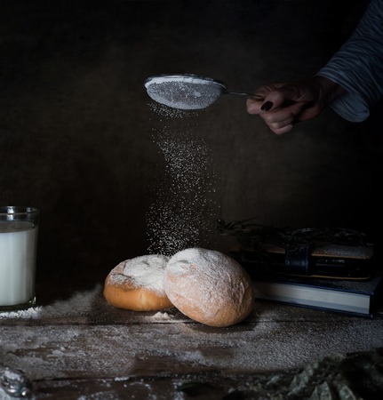 female hand sifts the flour on a wooden table. dark backgroundの写真素材