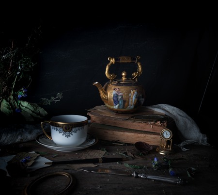 still life. vintage gold with enamel kettle, books and cup on the wooden table. dark background. space for textの写真素材