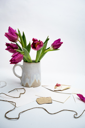 Pink tulips in a ceramic vase on a table with letters and envelopesの写真素材