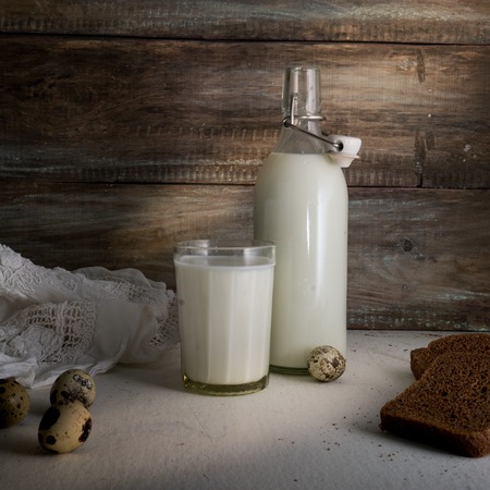 rustic still life with a bottle of milk, eggs and bread on background of rough wooden wallの写真素材