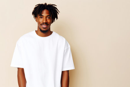 Cheerful young man with dreadlocks wearing a white t-shirt, against a beige background with copy spaceの素材