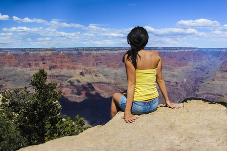 Young girl sitting on the edge of Grand Canyon National Park in Arizona, USA during sunny summer dayの写真素材