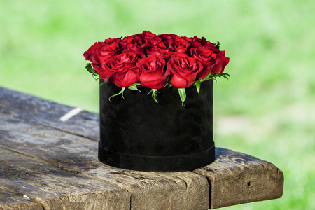 Beautiful bouquet of roses in a basket on a wooden table in natureの写真素材