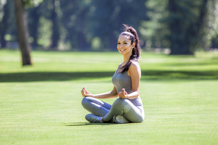 Young relaxed beautiful girl doing yoga exercises outdoor on a grass field during summer sunny daytimeの写真素材