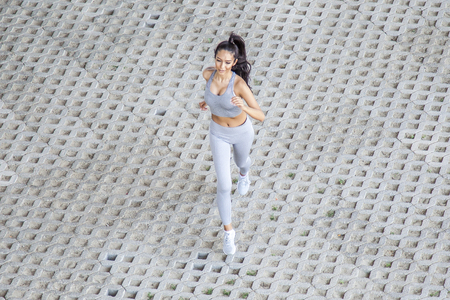 Young fit beautiful girl running outdoor on a pavement bricks during summer sunny dayの写真素材