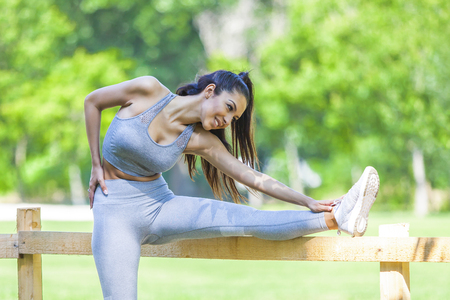 Young fit beautiful girl resting and stretching on a fence after running outdoor during summer sunny dayの写真素材