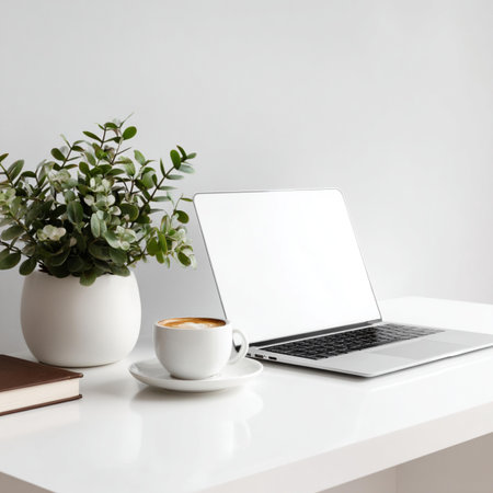 Modern workspace with laptop, coffee cup and plant on white desk.