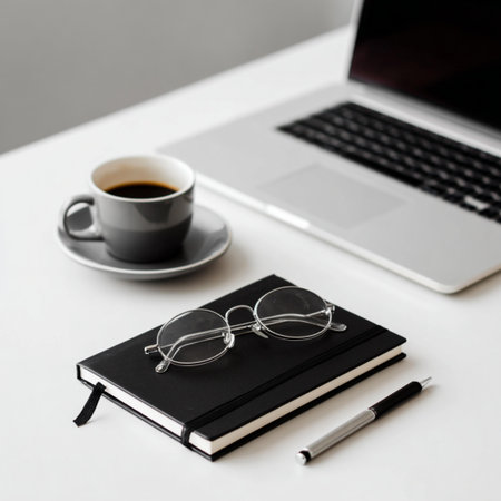 Laptop, glasses, notebook and coffee cup on white table.