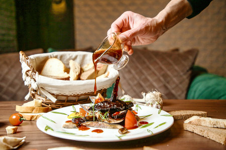 A person is pouring sauce onto a plate of food, creating a delicious and appetizing meal.の写真素材