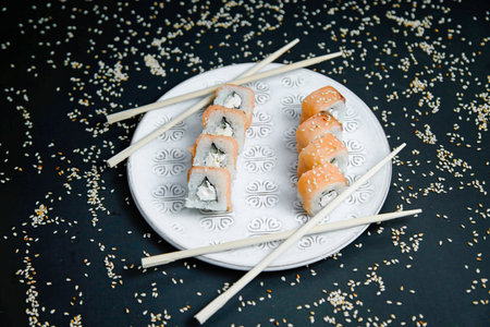 A white plate is topped with a variety of fresh sushi rolls, accompanied by a pair of chopsticks ready for consumption.の写真素材