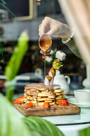 A person pours syrup onto a stack of golden-brown pancakes on a plate.の写真素材