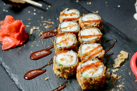 A close-up shot of a plate filled with a variety of fresh sushi, placed on a table alongside a pair...