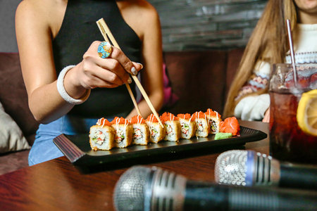 A person holds a pair of chopsticks over a plate filled with succulent sushi pieces.の写真素材