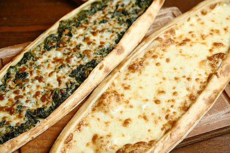 Two pizzas rest on top of a wooden cutting board.