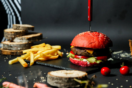 A photo showing a hamburger with a knife sticking out of it, accompanied by a serving of french fries.の写真素材