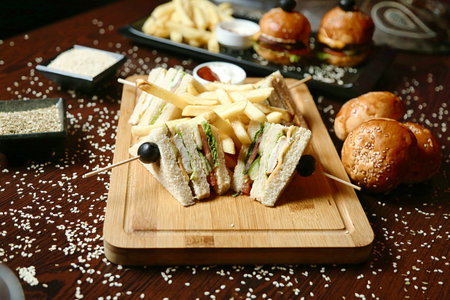 A wooden cutting board showcasing a delectable sandwich cut in half and served with golden French fries.の写真素材