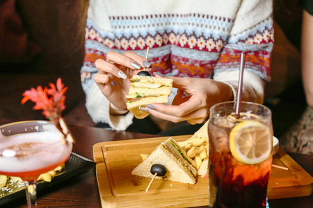 A woman sitting at an outdoor cafe, enjoying a sandwich and drinking a beverage.の写真素材