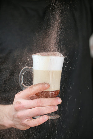 A person sprinkles sugar onto a cup of coffee, adding sweetness to their morning beverage.