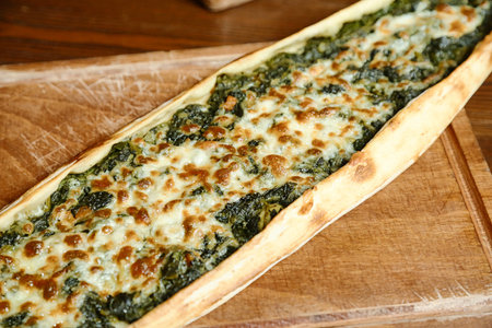 A freshly baked pizza topped with spinach and cheese placed on a wooden cutting board.の写真素材