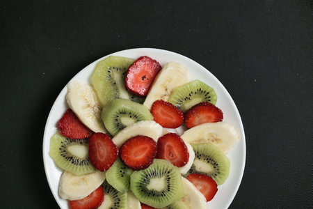 A white plate adorned with freshly sliced kiwi fruit and strawberries arranged neatly.の写真素材