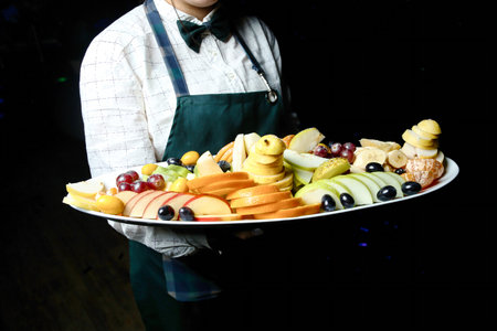 A man confidently showcases a tray filled with an assortment of delicious food items at an outdoor market.の写真素材