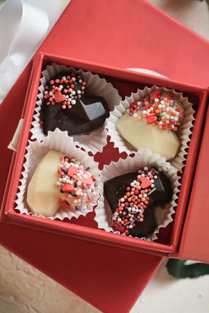 A box containing four heart-shaped chocolates adorned with colorful sprinkles.
