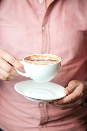 A man is seen holding a cup of coffee in a bustling city cafe.の写真素材
