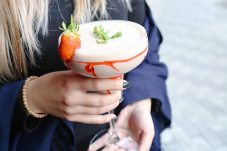 A woman gracefully holds a wine glass adorned with a vibrant strawberry.