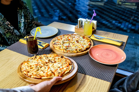 A photo of two pizzas placed on top of a wooden table.