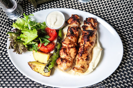 A white plate with a delicious arrangement of chicken and assorted vegetables, including carrots, broccoli, and bell peppers.の写真素材