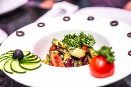 A white plate showcases a fresh salad topped with a single slice of cucumber.の写真素材