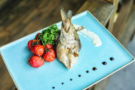 A blue plate is adorned with a freshly cooked fish, accompanied by vibrant tomatoes and crisp broccoli.の写真素材