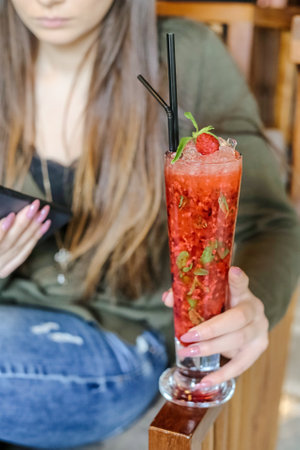 A woman dressed in casual attire holds a colorful cocktail drink while standing outside at a lively social gathering.の写真素材