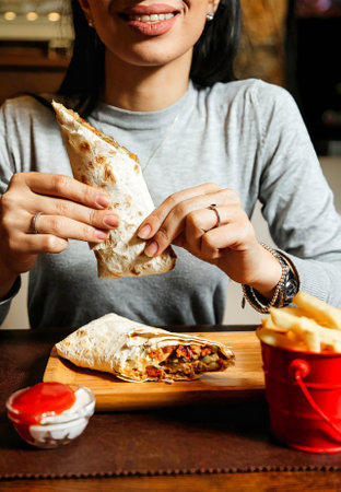 A woman is sitting at a table and eating a burrito.の写真素材